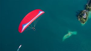 Das Bild zeigt den Gin Gliders Fuse 2. Bei dem Gleitschirm handelt es sich um einen Tandemschirm. Das Bild stellt den Schirm im Flug über einem See dar. Es handelt sich um einen Passagierflug oder auch Tandemflug. Das Photo wurden von oben aufgenommen.