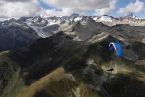 Das Bild ist das Titelbild für die Vorankündigung des Bonanza 2. Dies ist eine neuer XC Gleitschirm von Gin Gliders. Der Paragleiter befindet sich im Flug über den Bergen. Der Pilot sitzt in einem Liegegutzeug. Der Schirm ist in 6 Größen von XXS bis XL erhältlich.